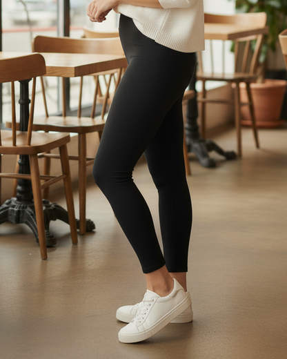 Woman standing in a modern cafe with wooden furniture and large windows.